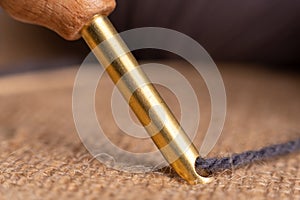 Macro photography of a golden 5 millimeter punch needle stitching in a burlap fabric with a grey wool