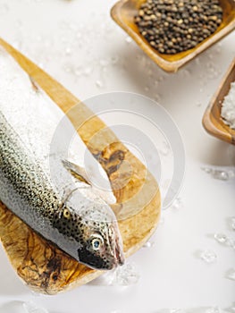 Macro photography. One fresh fish on a wooden cutting board. In the background, salt and spices in wooden bowls. White background