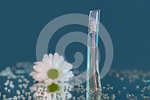 Macro photography of a transparent bottle of perfume standing on a mirror near a beautiful white flower among rhinestones