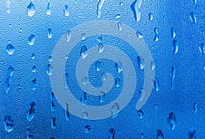 Macro photography of water drops on glass window blue background after the rain.