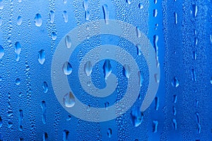 Macro photography of water drops on glass window blue background after the rain.