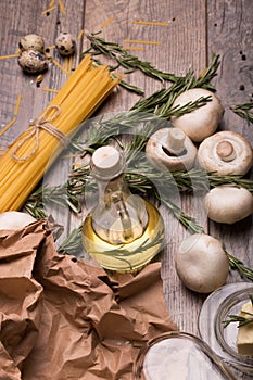 Macro picture of noodles, mushrooms, eggs, oil bottle, garlic and rosemary. Uncooked ingredients on a wooden table