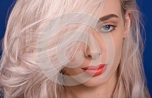 Macro of Platinum Blonde Hair Woman With Blue Eyes and Augmented Lips, Painted With Coral Lipstick, With an Eye Covered with Hair