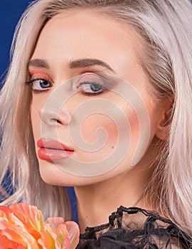 Macro of Platinum Blonde Hair Woman With Blue Eyes and Augmented Lips, Painted With Coral Lipstick and Orange Flower