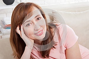 Macro portrait of smiling female face. Attractive and beautiful middle aged woman sitting on sofa and relaxing at home. Menopause.