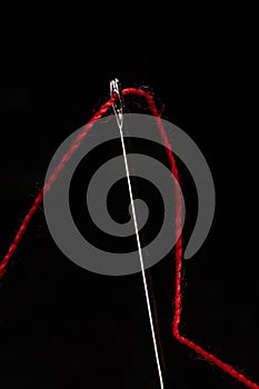 Macro of a red thread through the eye of a needle
