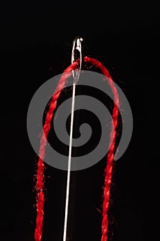 Macro of a red thread through the eye of a needle