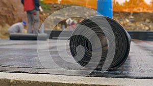 MACRO: Roll of tar lies on the ground as contractors work in the background.