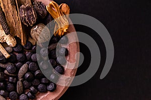 Macro shot of black ayurvedic pills placed with dried herbs and spices on black background. Unani medicine concept