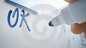 Macro Shot of a Blue Marker Pen Being Held with a Hand. Person Wrote OK on a Whiteboar