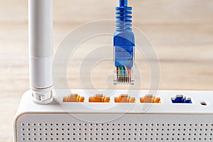 Macro shot of blue network cable plug is almost inserted into the yellow socket of white wi-fi wireless router. Wlan router for