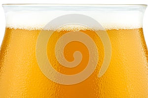 Macro shot of cold beer in a Teku tasting glass filled to full with foam, drops of water on glass, the upper part of the glass is