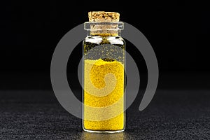Macro shot of curries spice in a small glass bottle closed with a cork, isolated on a black background,