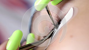 Macro shot of the eyelash extension procedure, the master glues the eyelash with tweezers