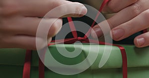 Macro shot of female hands tying red ribbon bow on green paper gift box