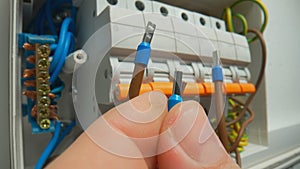 A macro shot of the fingers of a man who is holding a brown wires with blue bushing ferrules. High voltage electrical