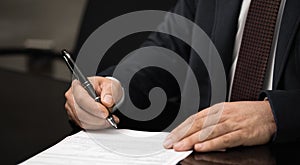 Hand of a businessman signing or writing a document on a sheet of white paper using a nibbed fountain pen.