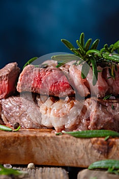 Macro shot of medium rare grilled juicy beef steak ribeye with rosemary on wooden cutting board on dark blue background. photo