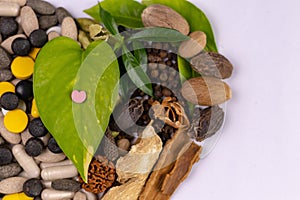 Macro shot of one pink heart shaped tablet on a green leaf with herbs in the white background. herbal medicine concept