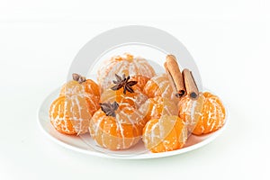 Macro shot of peeled juicy tangerines decorated with star anise spice and cinnamon sticks on the white plate isolated on white.