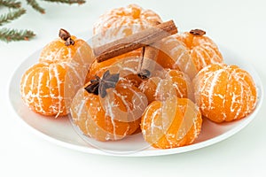 Macro shot of peeled juicy tangerines decorated with star anise spice and cinnamon sticks on the white plate isolated on white.