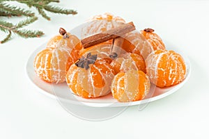 Macro shot of peeled juicy tangerines decorated with star anise spice and cinnamon sticks on the white plate isolated on white.