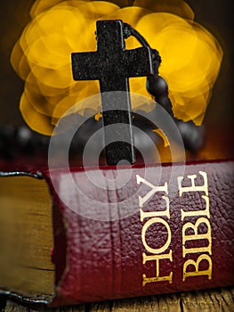 Macro shot. The red book of the Holy Bible and the Catholic cross on a bright yellow background. Symbols of faith, spirituality.