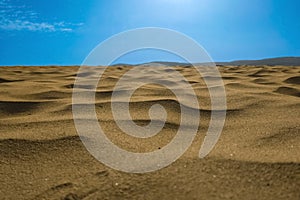 Macro shot of sand surface against blue sky background with small clouds and sun halo. Unique natural areas such as