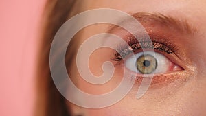 Macro shot of scared surprised green woman eye with eye shadow isolated on pink background