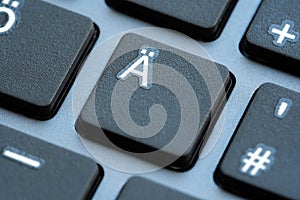 A macro shot showcasing the Ã„ with diaeresis key button on a black computer keyboard, with surrounding keys softly blurred,