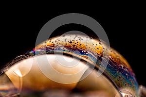 Macro shot of a soap bubble with a colorful texture isolated against a black background