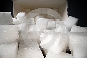 Macro shot of sugar cubes next to carton box on wooden table. Unhealthy food sweetener, sweet crystal cubes