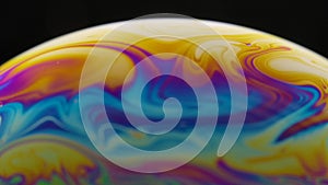 A macro shot of the surface of thin film of soap with rainbow colors creating a beautiful swirling effect. Semicircle of