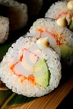 Macro shot of tasty sushi roll futomaki with avocado, crab meat and tobiko caviar on wooden serving board