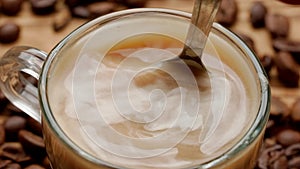 Macro shot of a teaspoon stirring milk in a cup of coffee or tea. The spoon is lowered into the drink and stirred. A