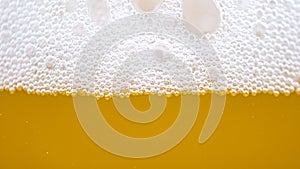 MACRO: Tiny bubbles form the foam on top of a glass full of pale ale beer.