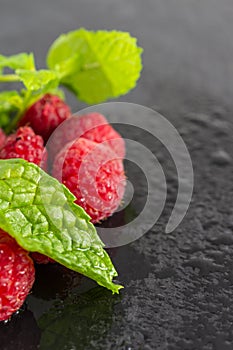 Macro top view of mint leaf and wet raspberries out of focus on black slate in vertical