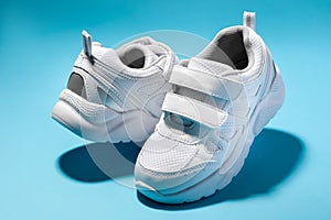 macro of two white children's floating sneakers with velcro facing each other isolated on a blue background