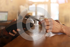 Macro unknown hand giving terminal to visitor for mobile phone payment indoor. Client hand paying bill with smartphone