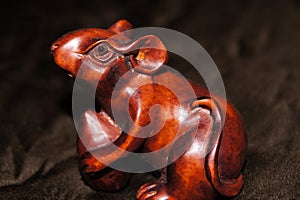 Macro view of a cute wooden carved polished brown mouse on a dark material.