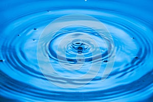 Macro view of drops making circles on blue water surface isolated on background.