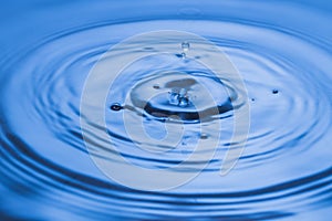 Macro view of drops making circles on blue water surface isolated on background.