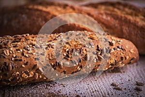 Macro view of fresh crunchy baguette bread with sunflower seeds and other seeds on the rustic wooden desk