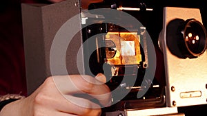 Macro view of hands inserting frame with film into slide projector and fingers spinning a wheel