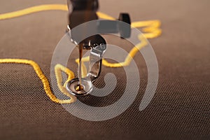 macro view on needle and foot of an embroidery machine stitching a golden ox symbol on brownish shiny olive fabric photo