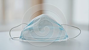 Macro view of a single disposable surgical mask resting on a clean table surface