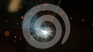 MACRO: Welder working in his workshop makes a weld on the dark metal surface.