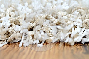 Macro of white shaggy carpet on brown wooden floor