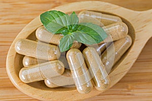 Macro of wooden spoon full of herbal medicine in clear capsules, ideal for Homeopathic remedies