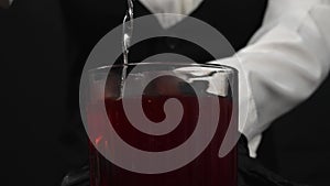 Macrography of a female bartender pour red syrup in glass with ice. Comestible.